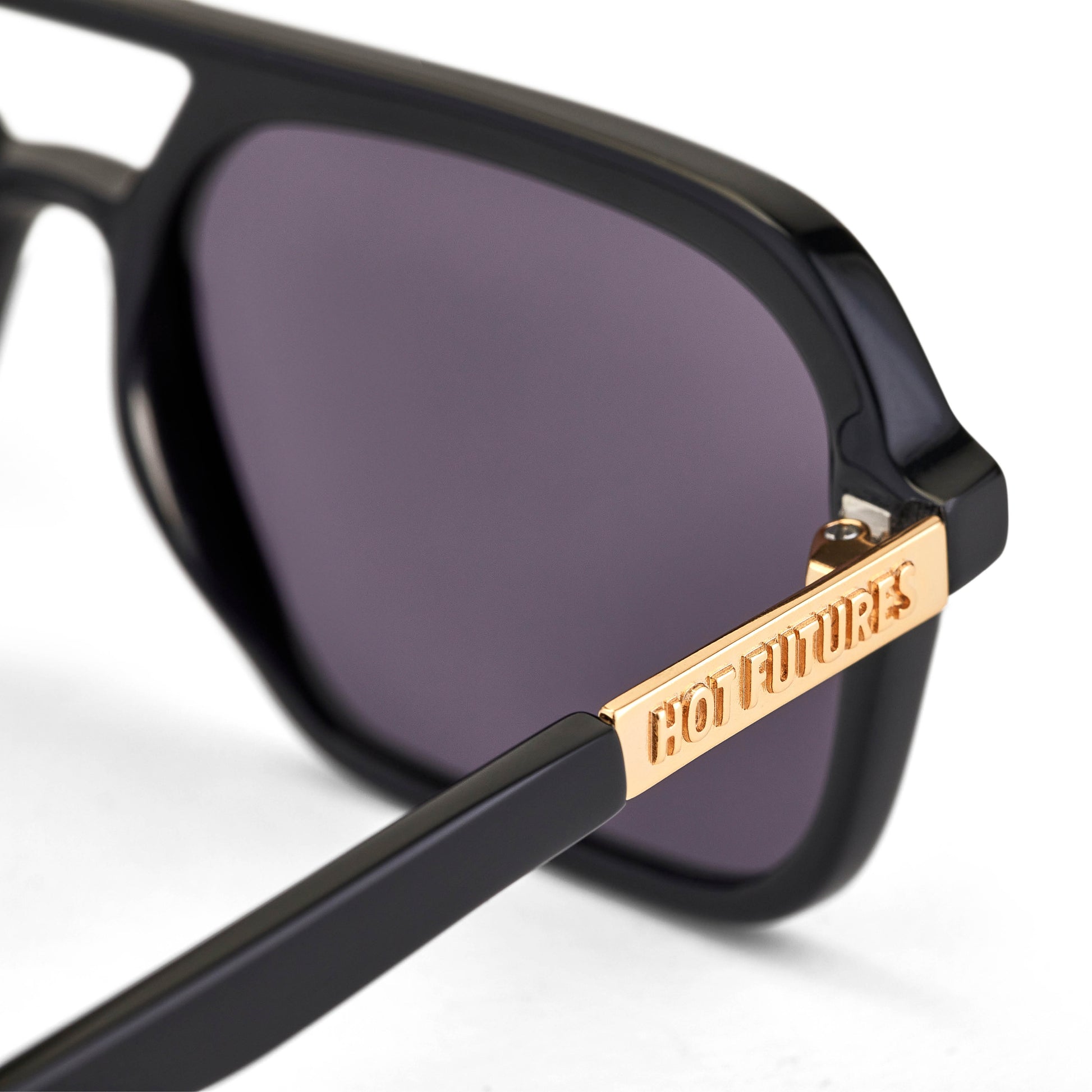 A pair of gloss black aviator sunglasses with smoky black lenses by Hot Futures. With the gold text branding to the arms