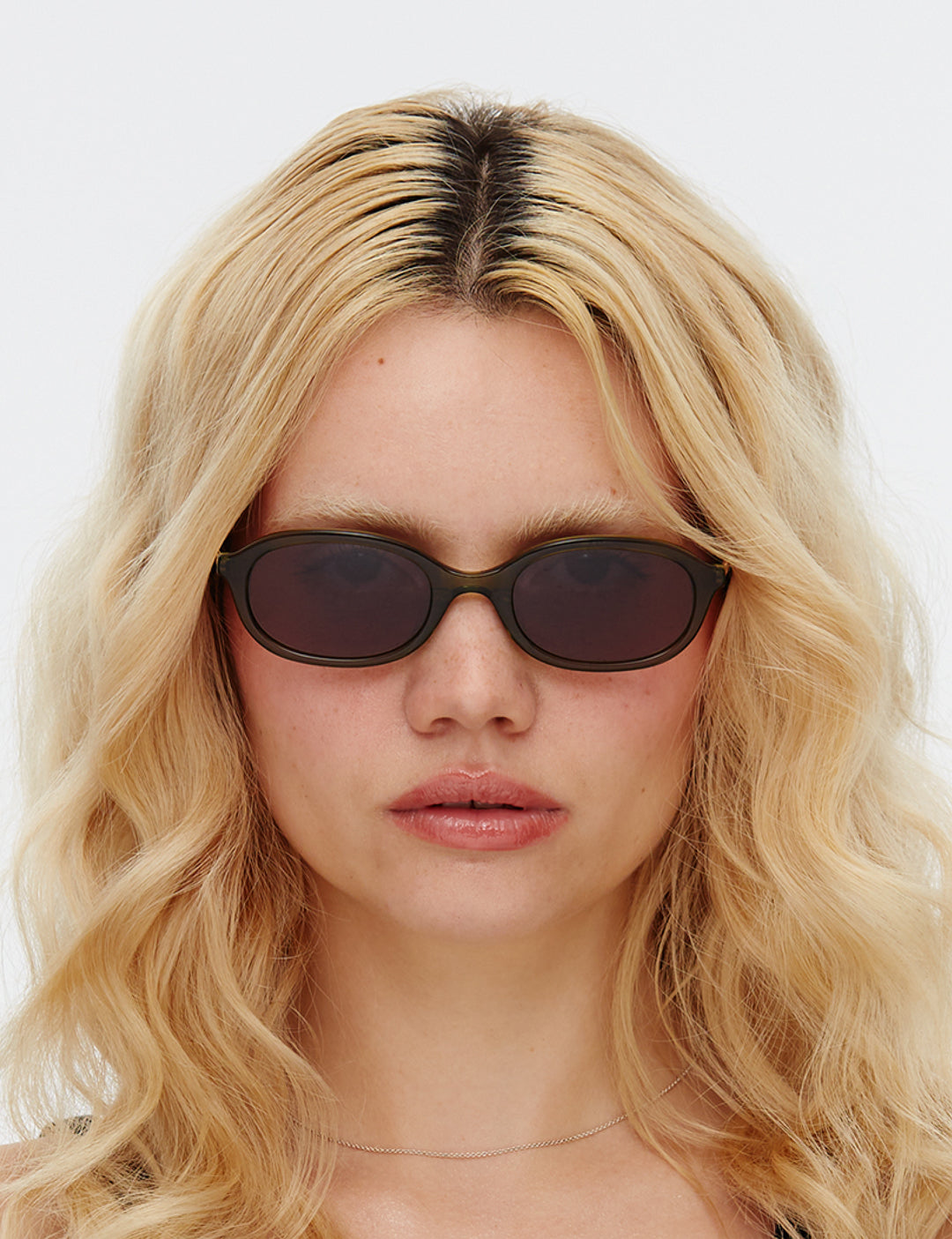 Olive green oval-shaped sunglasses with dark green lenses, displayed against a white background.